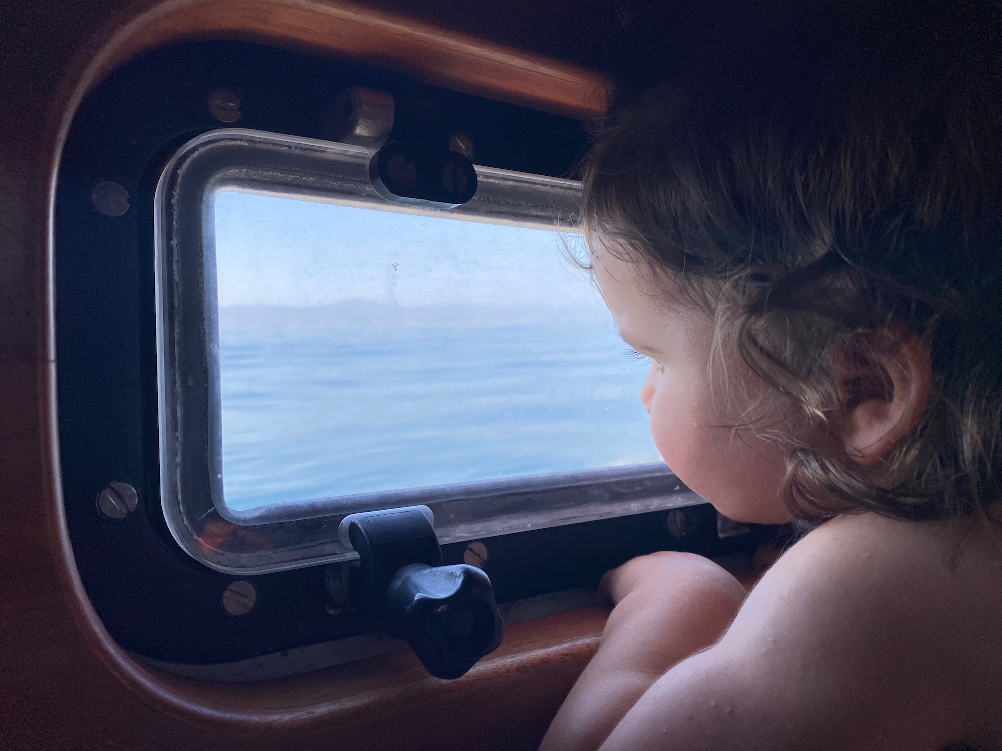 Toddler looking out the window of a sailing boat while travelling